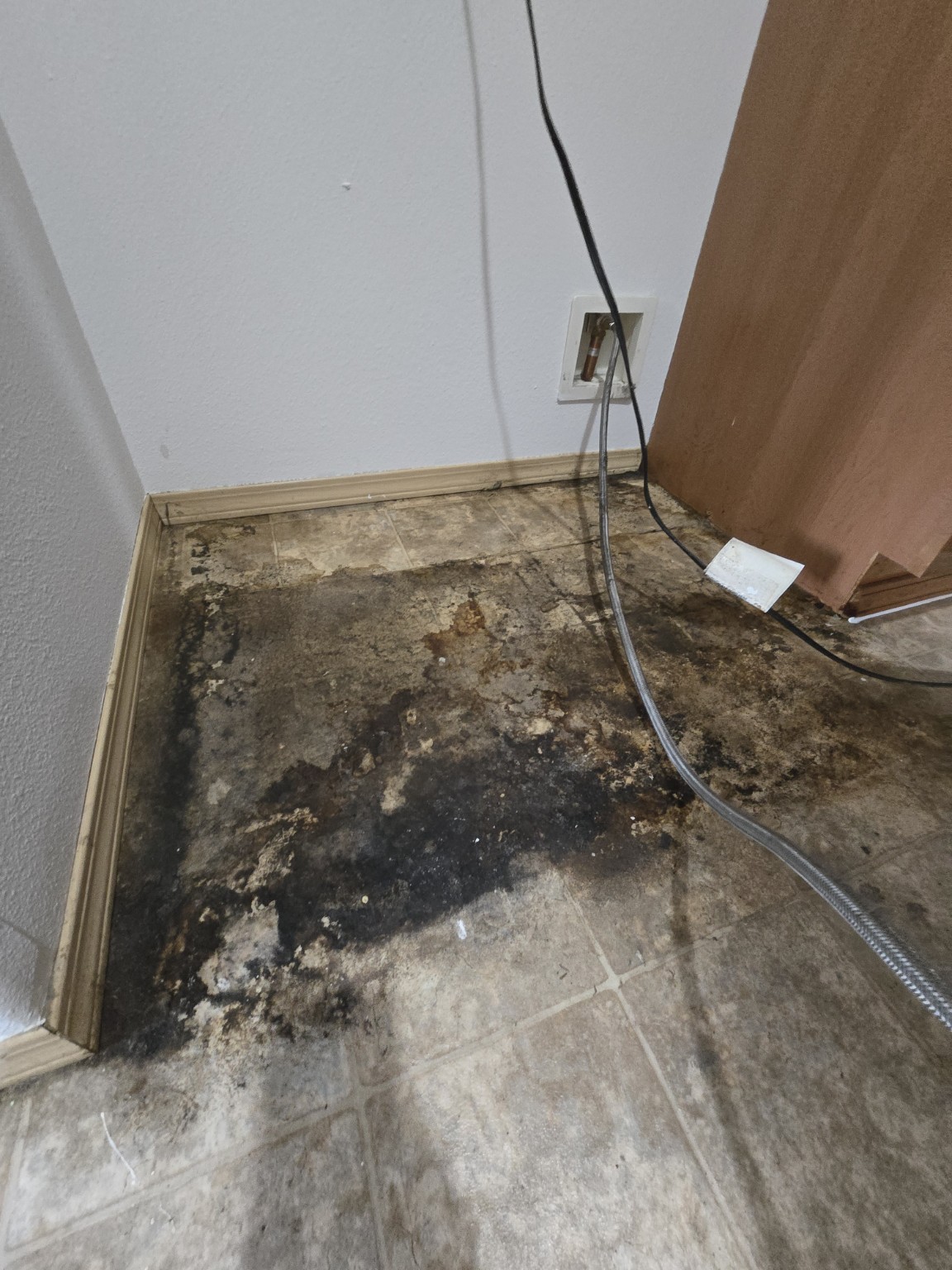Floor behind the refrigerator with heavy dark buildup before cleaning